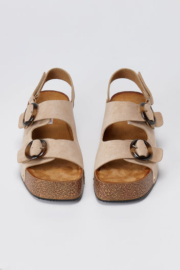 Pair of taupe suede sandals with two straps, gold ring buckles and tan cork-look footbed, front view on light grey