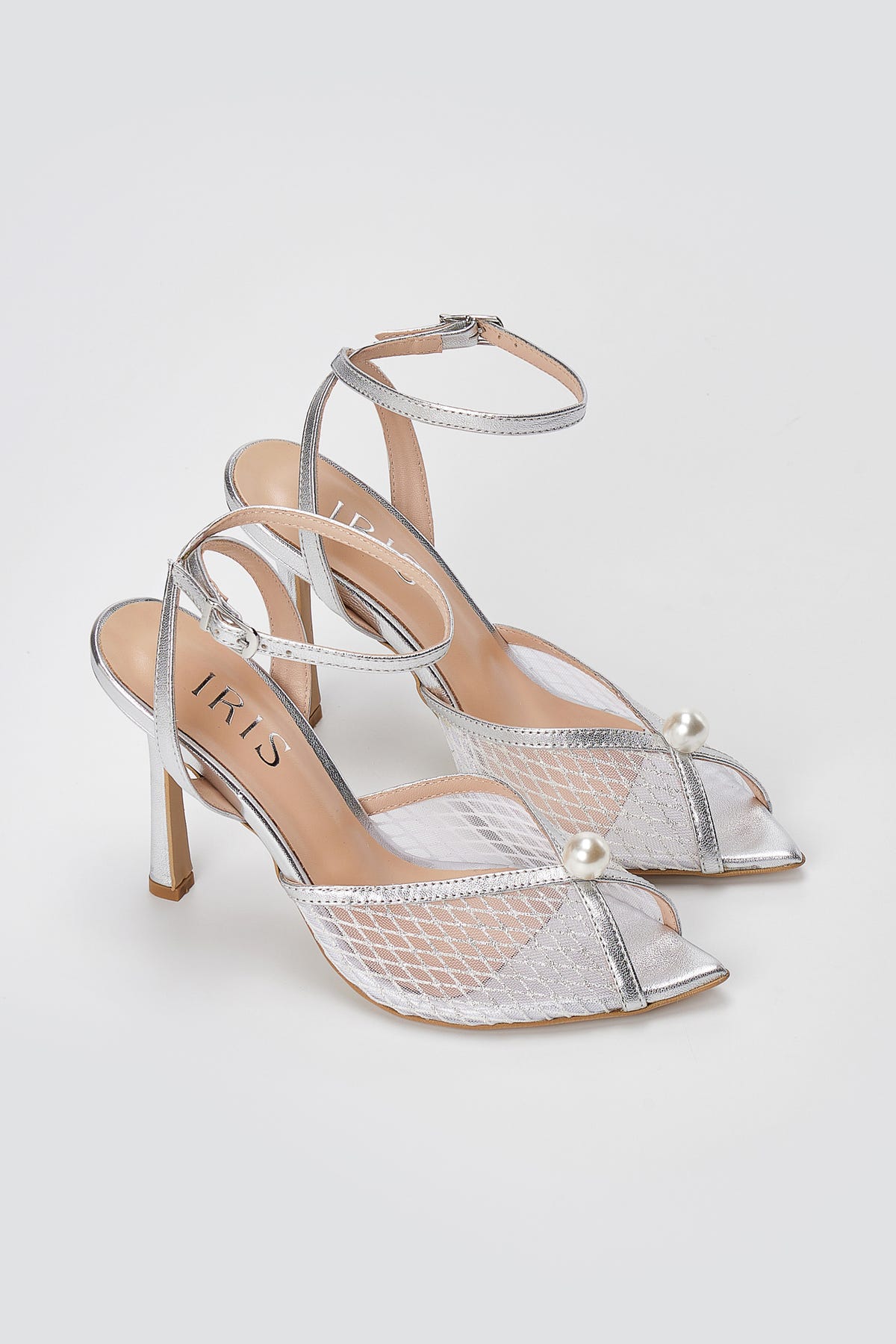 Pair of silver metallic sandals with mesh peep toes, pearl beads, ankle straps and slim high heels, three-quarter view