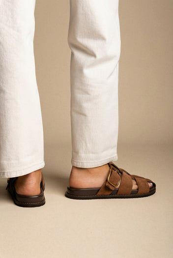 Brown suede cage-strap slides with a large gold buckle, worn with white jeans, back and side view on a model