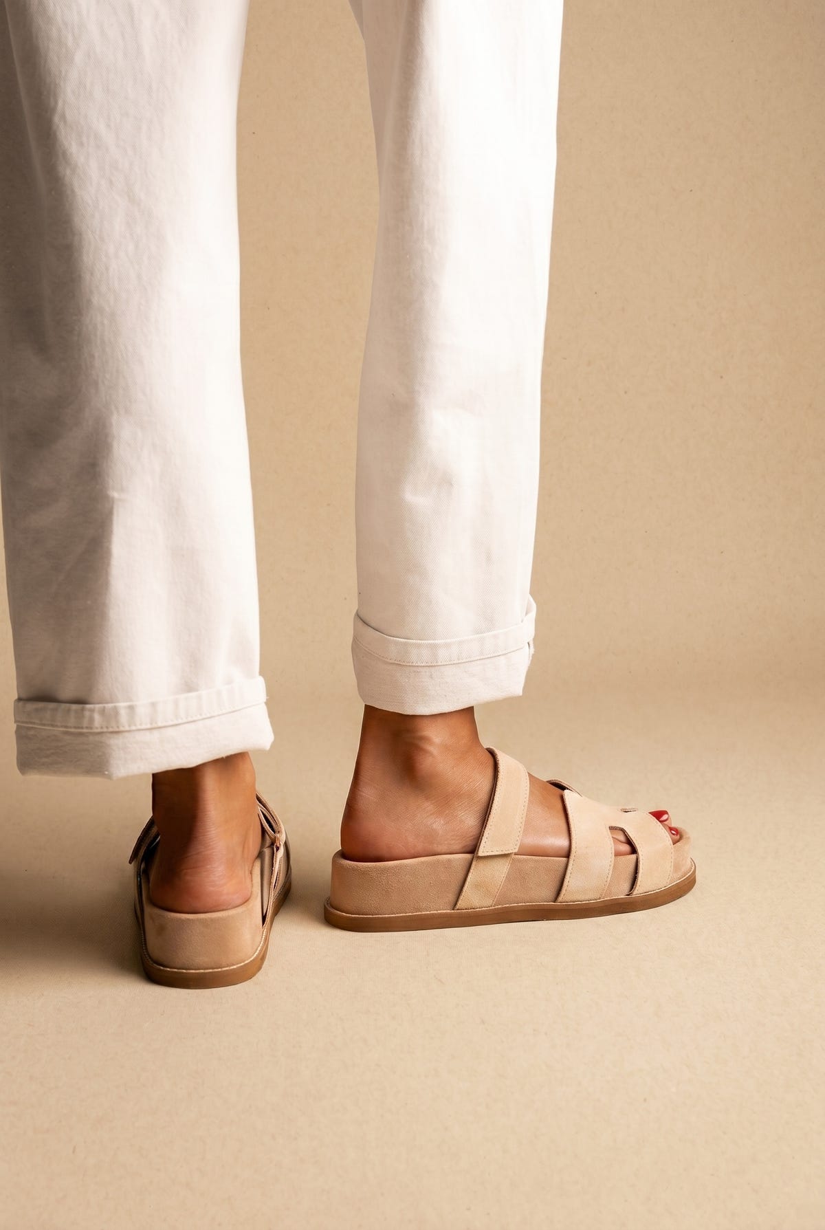 Back view of beige suede chunky slide sandals with wide straps and a thick sole, worn with white jeans on a model
