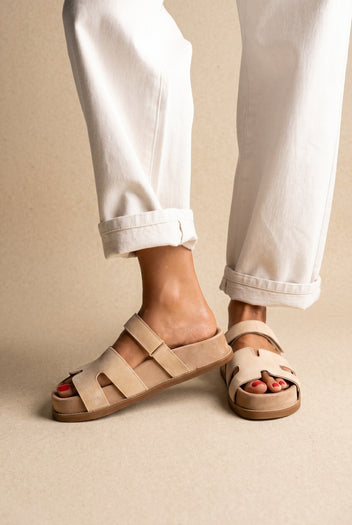 Beige suede chunky slides with cut-out straps and thick sole, front view on a model wearing rolled white jeans