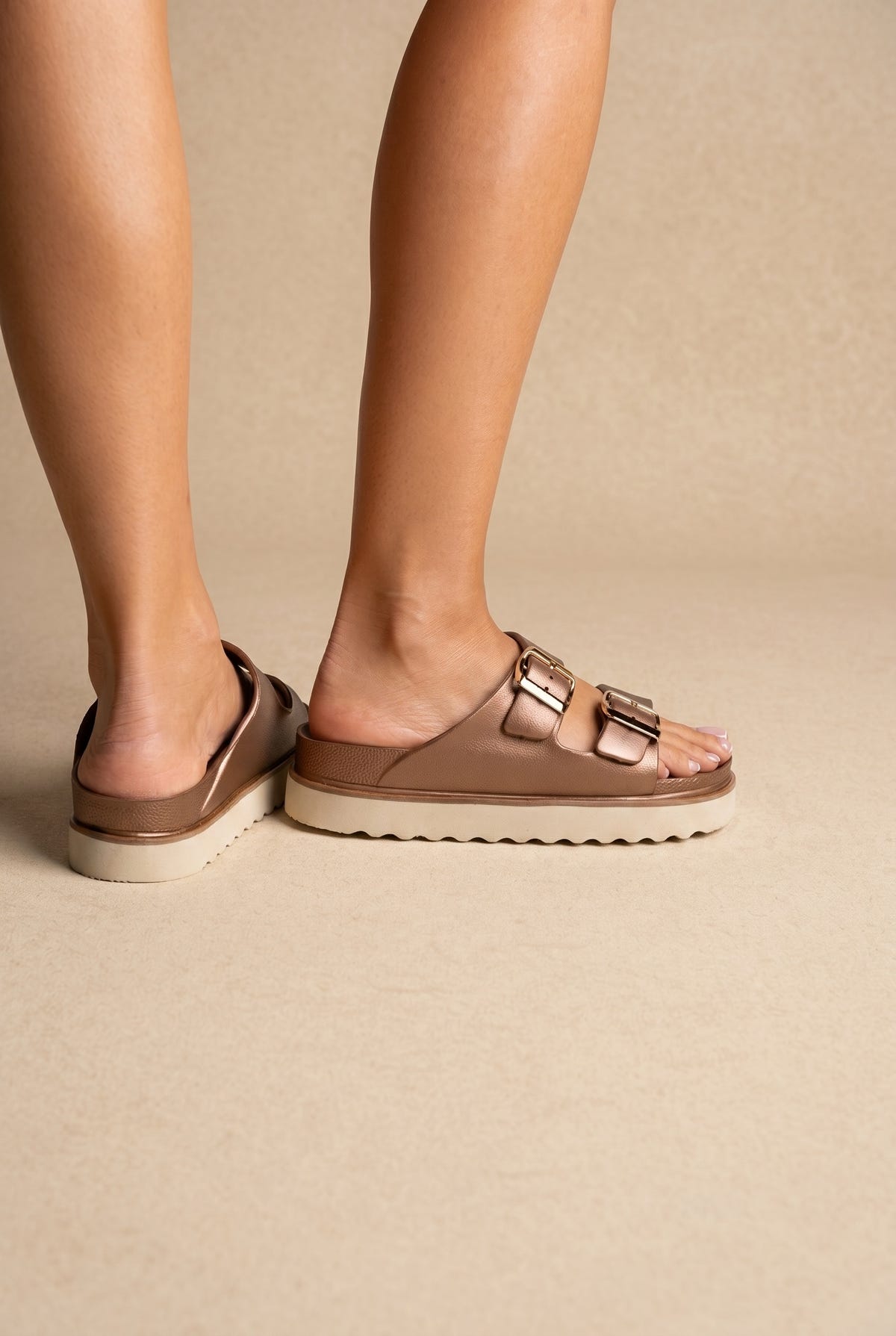 Metallic rose gold leather slide sandals with two buckled straps and white ridged platform sole, side view