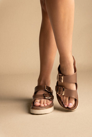 Metallic rose gold leather double-buckle slides with cream platform sole, front view on a model