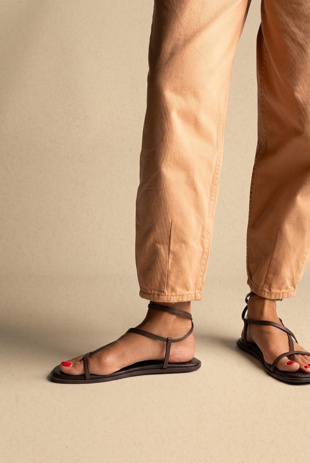Dark brown leather flat strappy sandals with thin straps and ankle strap, side view on a model