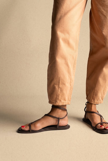 Dark brown leather flat strappy sandals with thin straps and ankle strap, side view on a model