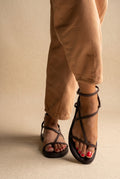 Dark brown leather flat strappy sandals with thin straps and ankle buckle, front view on a model