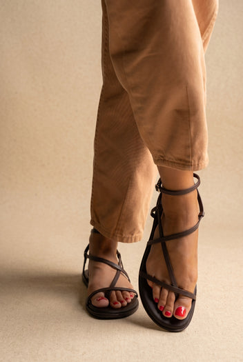 Dark brown leather flat strappy sandals with thin straps and ankle buckle, front view on a model
