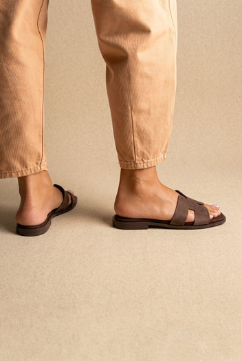 Dark brown flat H band slides with brown flat sole, back and side view on a model in tan trousers