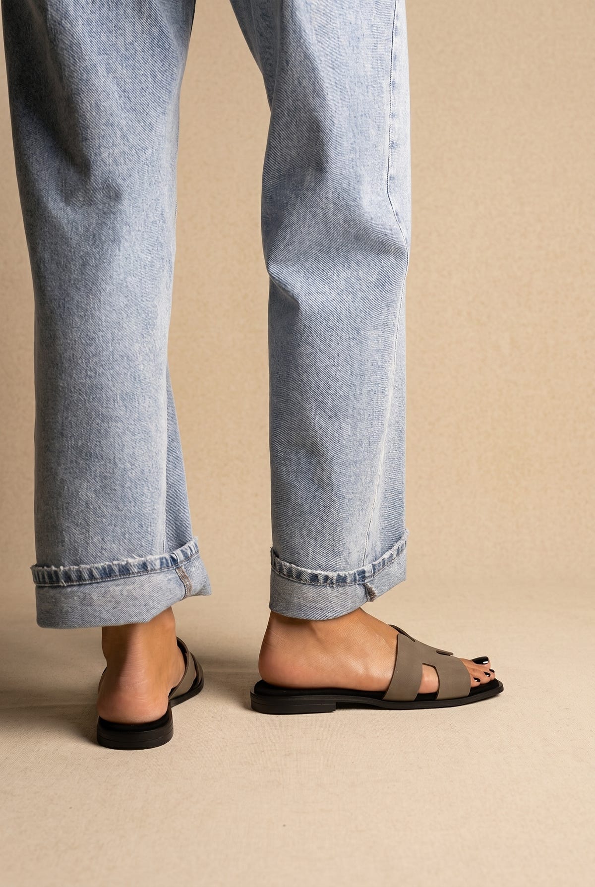Taupe grey H band flat slides with black sole, back and side view on a model in light blue jeans