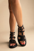 Black leather gladiator sandals with multiple ankle straps, ring buckles and chunky sole, front view on a model