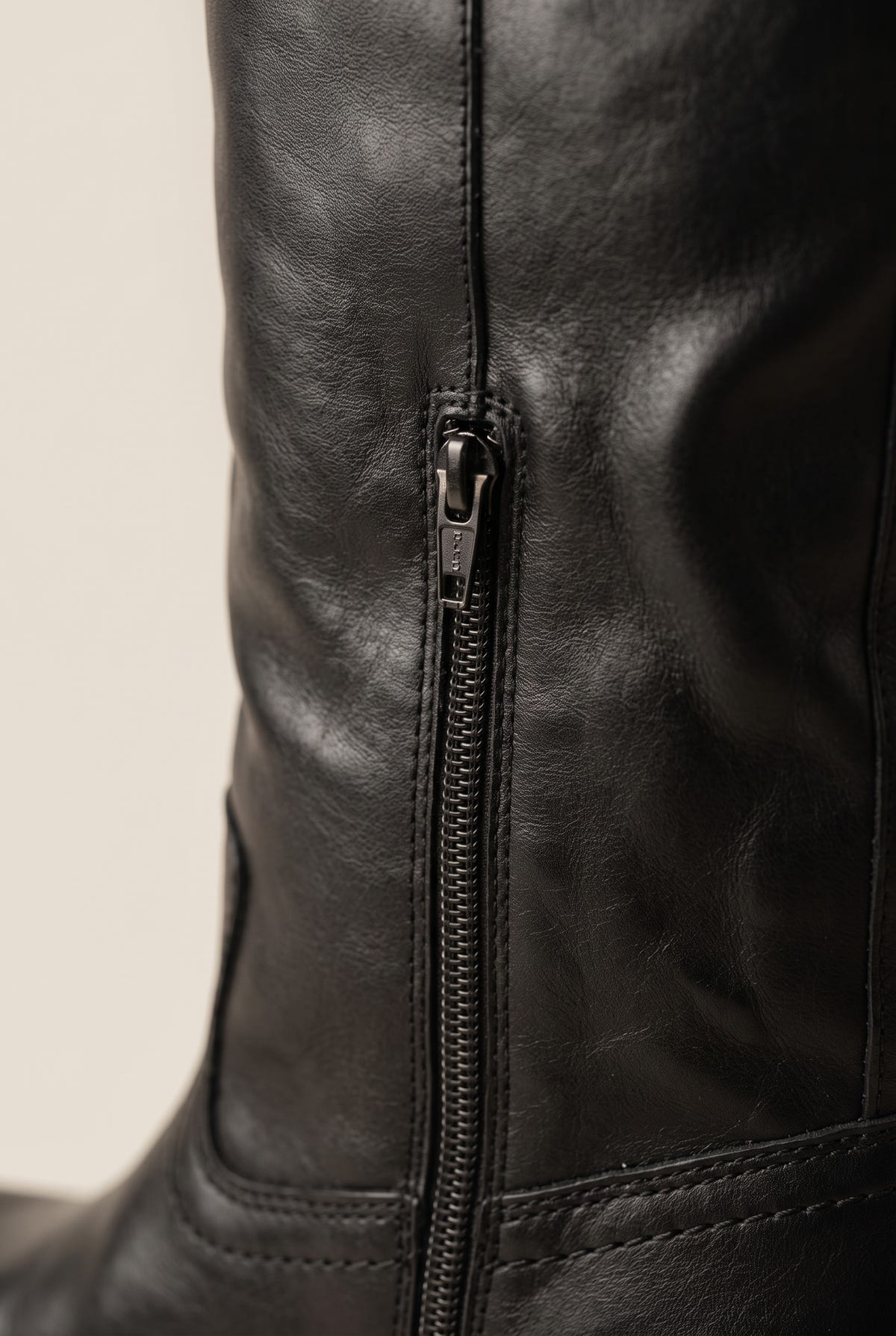Close-up of black smooth leather boot shaft with a metal side zip and visible topstitching
