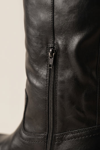 Close-up of black smooth leather boot shaft with a metal side zip and visible topstitching