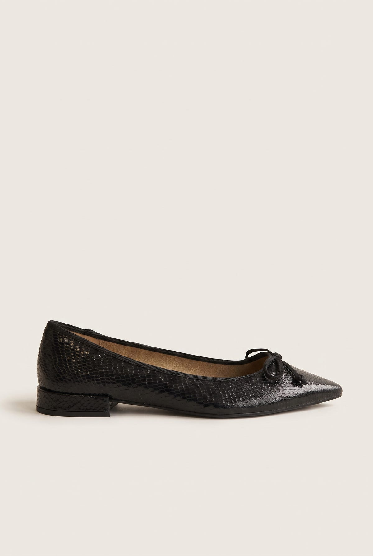 Side view of black snake-embossed leather pointed ballet flat with bow at toe and low block heel on white