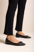 Black snake-embossed leather pointed flats with small bows and low heels, side view worn on model