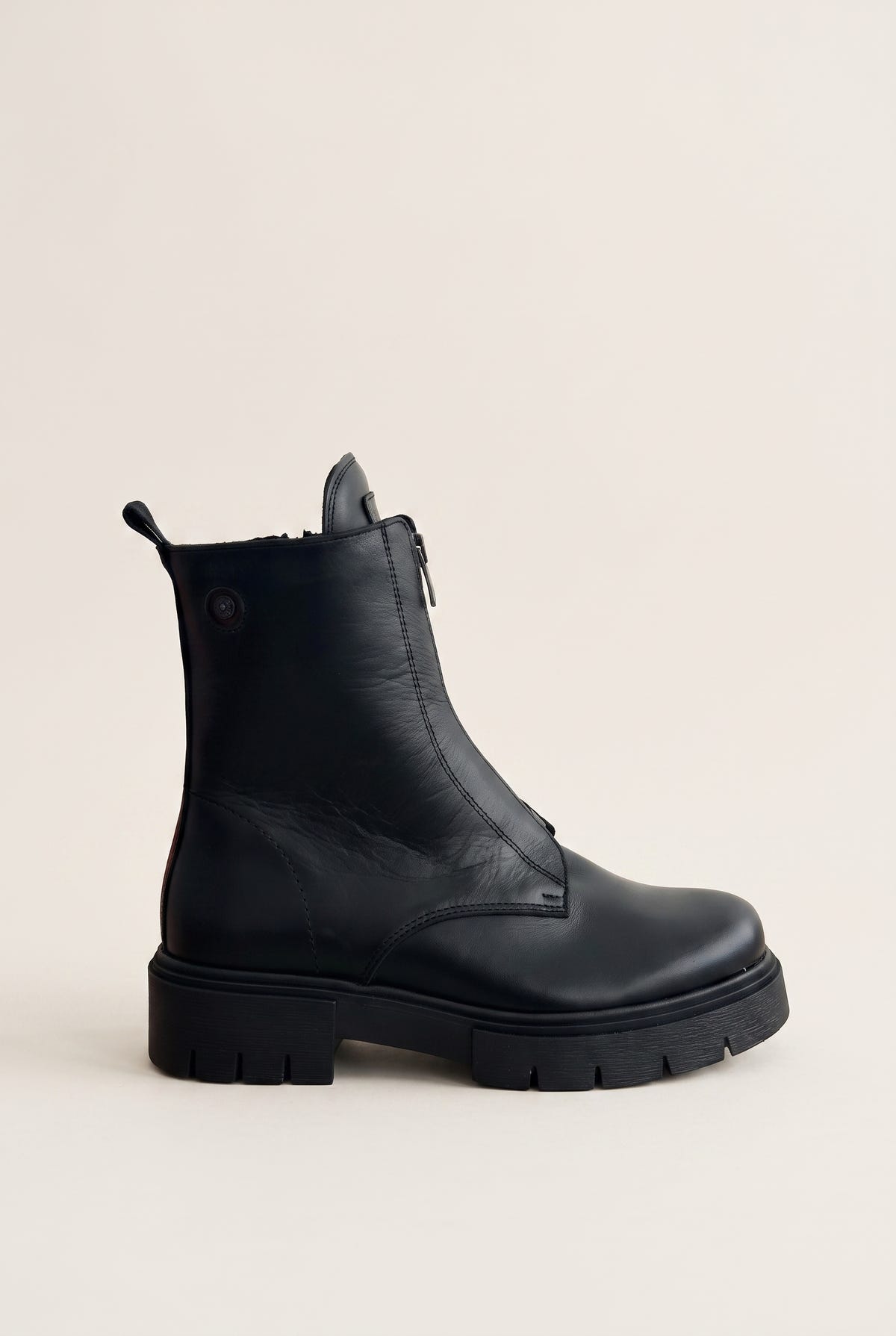 Black leather lug-sole ankle boot with front zip, angled side view on a light grey background