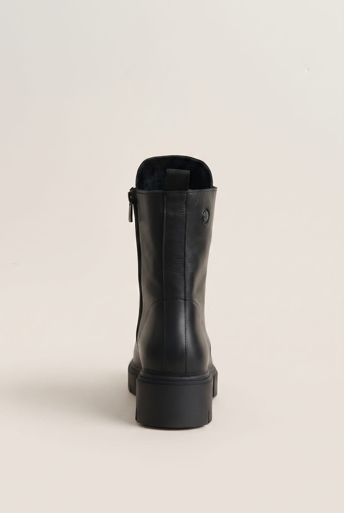 Black leather ankle boot with lug sole and side zip, single boot in front view on a light beige background