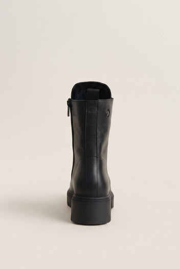 Black leather ankle boot with lug sole and side zip, single boot in front view on a light beige background