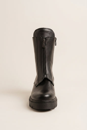 Black leather knee-high boots with lug sole and back zip, front view on a light beige background