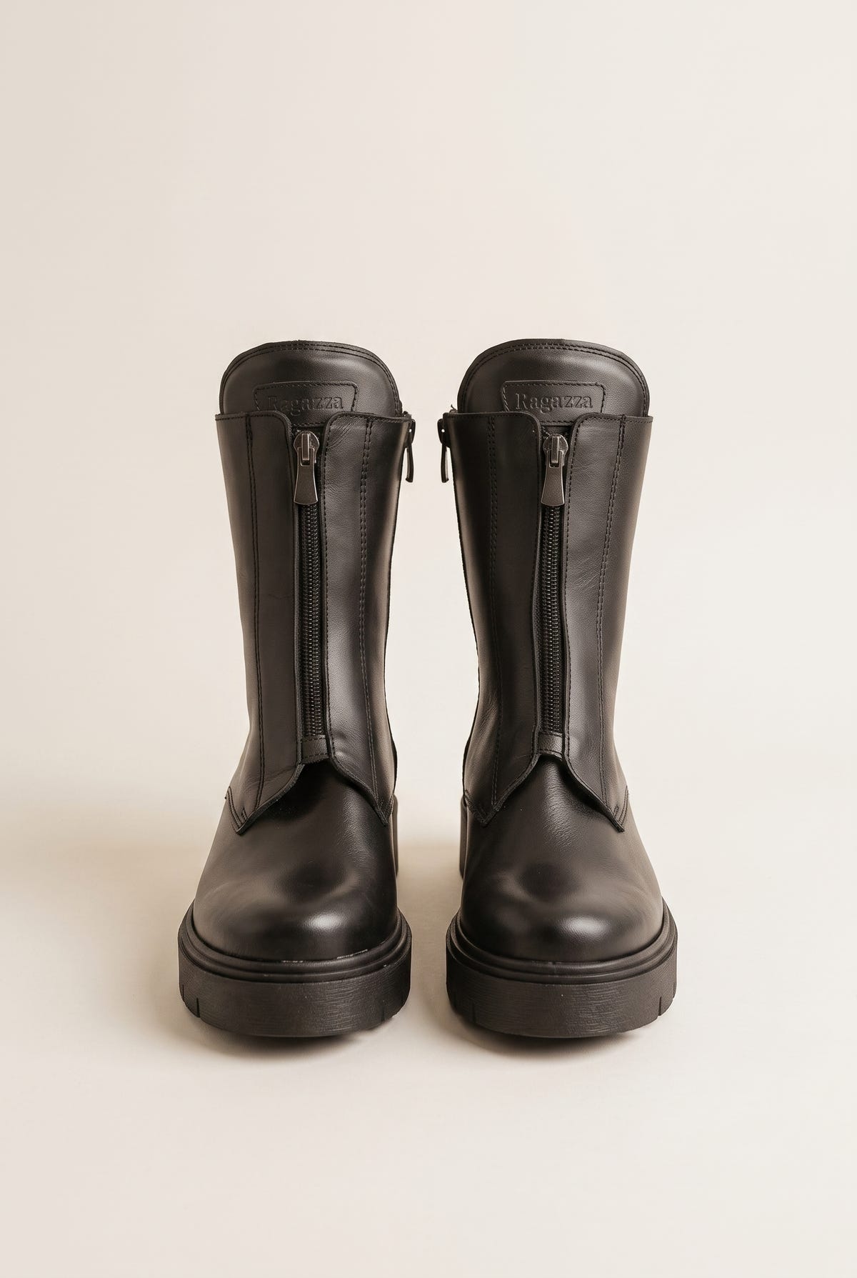 Black leather lug-sole boots with front zip, pair in top-down view on a light beige background