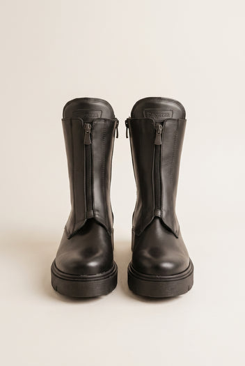 Black leather lug-sole boots with front zip, pair in top-down view on a light beige background