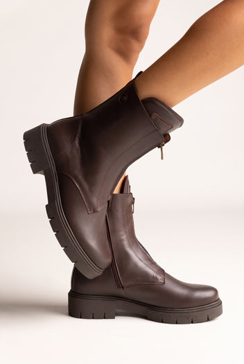 Brown leather lug-sole ankle boots with elastic side panels, angled view on a model's legs in studio light