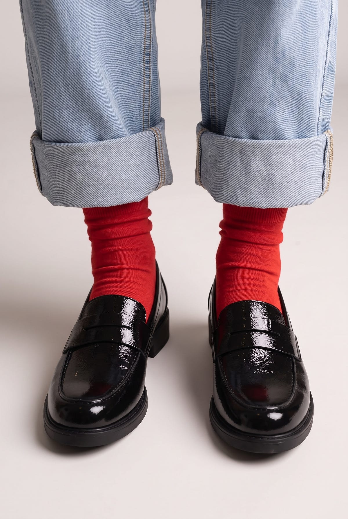 Black glossy patent leather penny loafers with strap detail and chunky flat lug sole, front view worn on model
