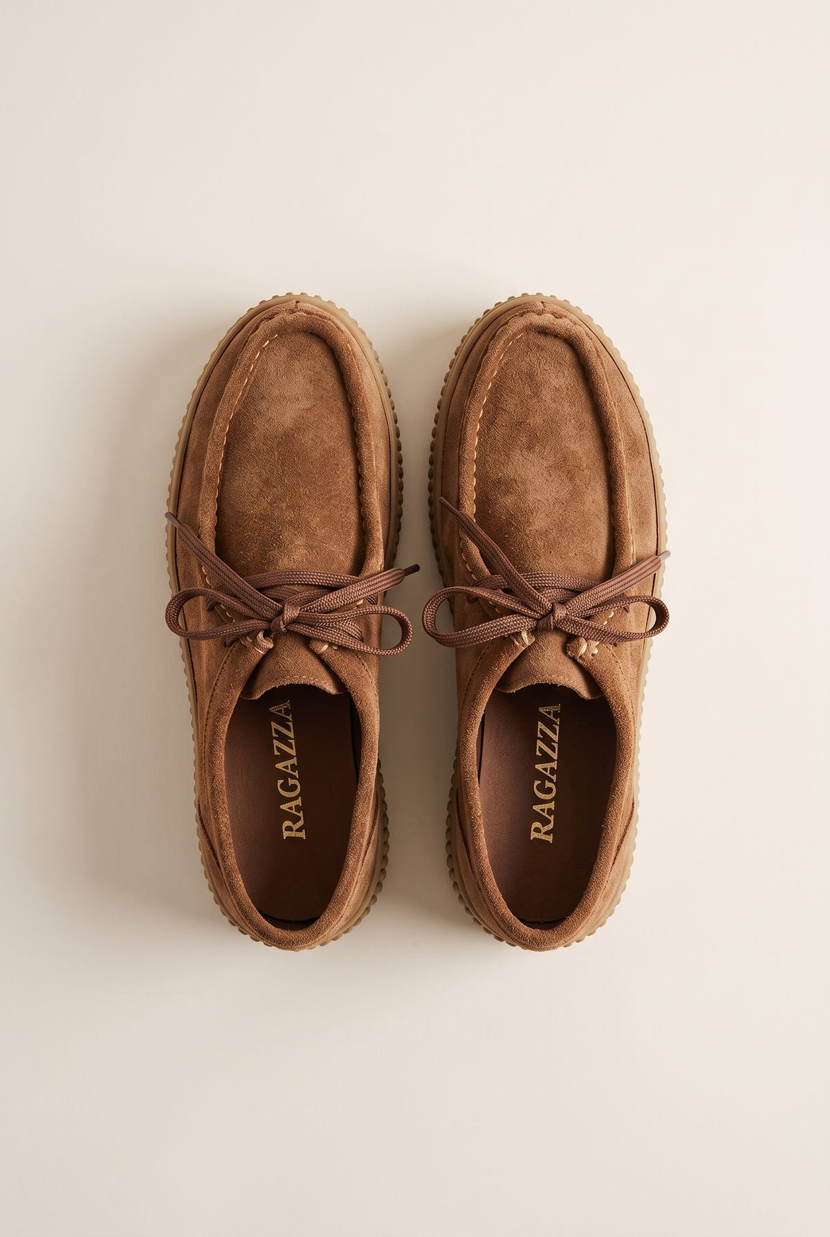 Tan suede lace-up creeper shoes with crepe rubber sole, pair in top-down view on a light beige background