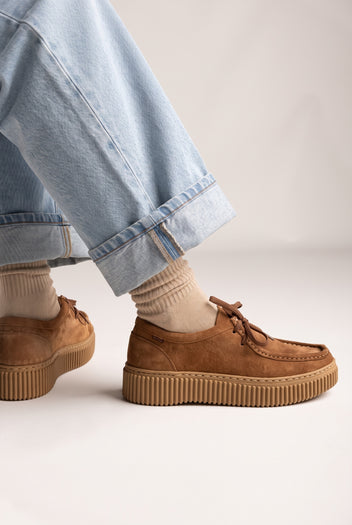 Tan suede moccasin lace-up shoes with stitched toe detail and chunky ridged crepe-style sole, side view, worn on model