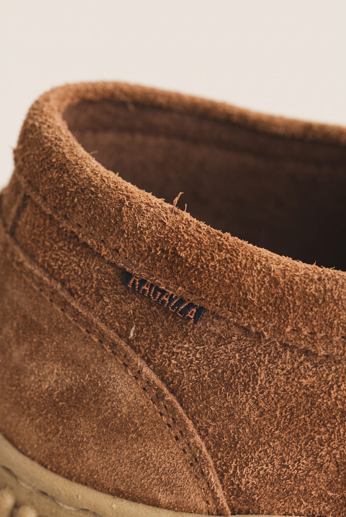 Close-up of tan suede shoe collar and crepe rubber sole, detail view on a light beige background