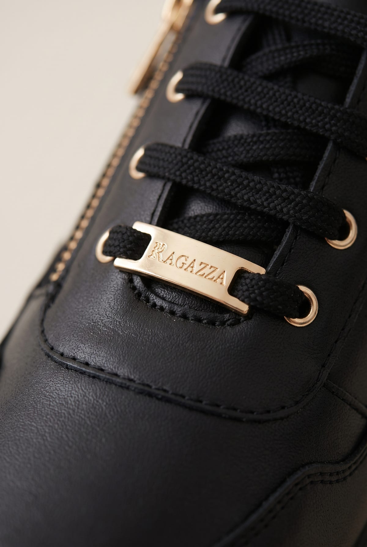 Close-up of black leather lace-up wedge sneaker with gold eyelets, gold lace tip and side zip