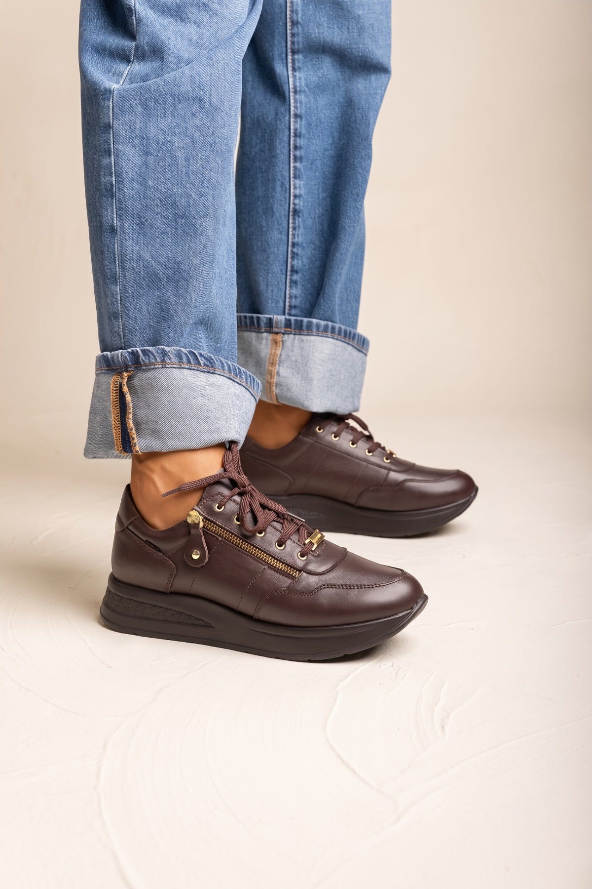 Model wearing cuffed wide leg jeans with brown leather lace up wedge sneakers and thick rounded sole in a side view