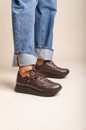 Model wearing cuffed wide leg jeans with brown leather lace up wedge sneakers and thick rounded sole in a side view
