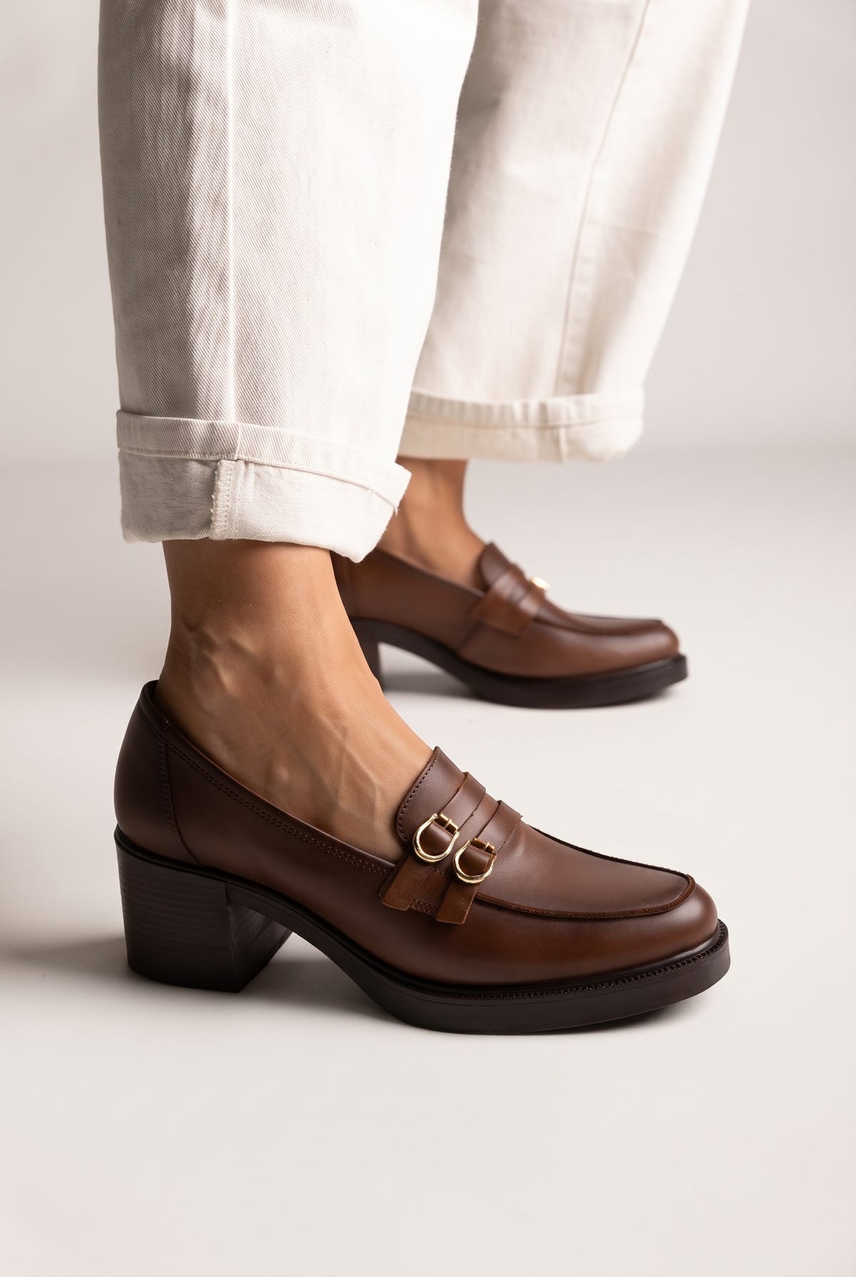 Brown smooth leather block heel loafer with gold double buckle straps and thick black sole, side view, worn on model