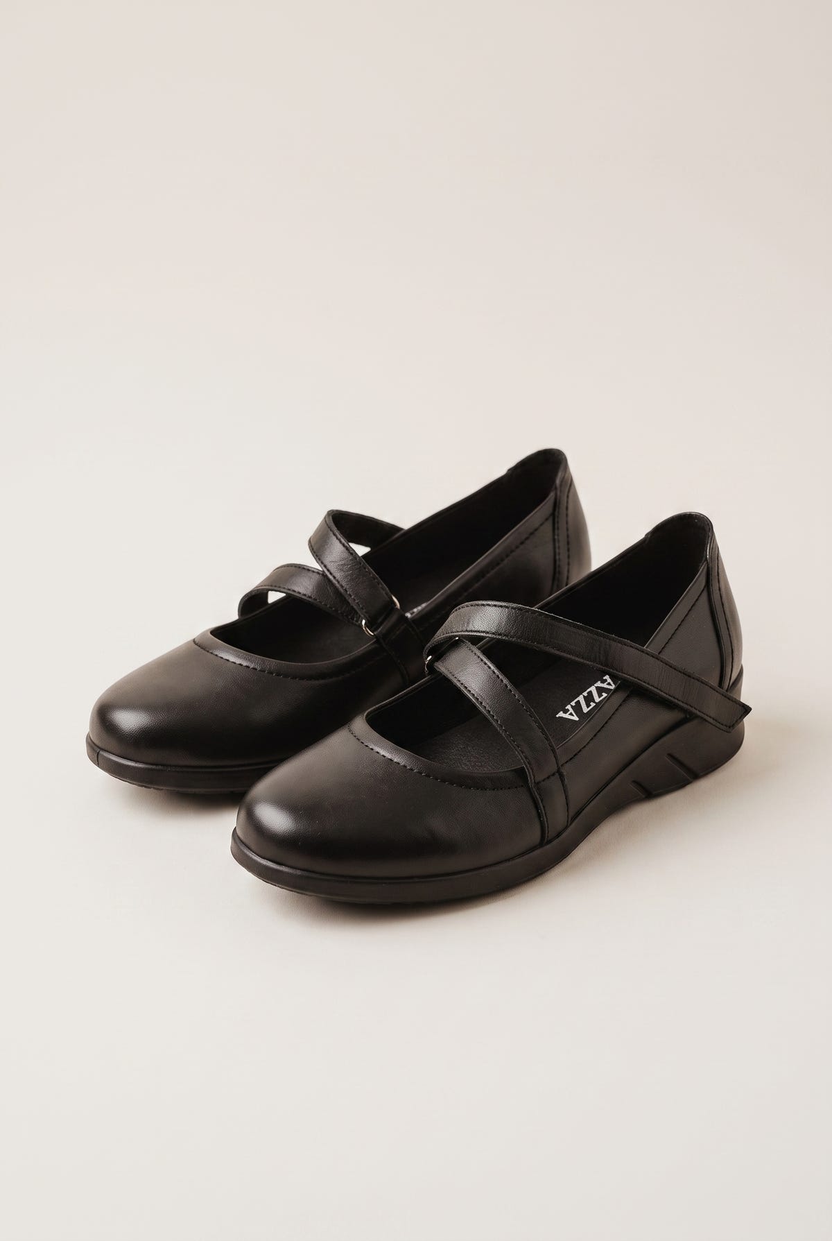 Pair of black leather Mary Jane flats with crossover velcro straps and flatform soles, angled view