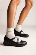 Black leather Mary Jane shoes with crossed straps, rounded toe and chunky sole, worn on model, side view