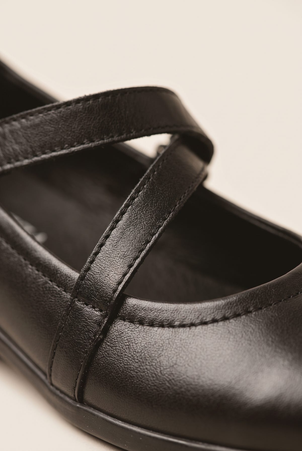 Close-up of black leather ballet flat with crossover strap, rounded toe and smooth leather finish