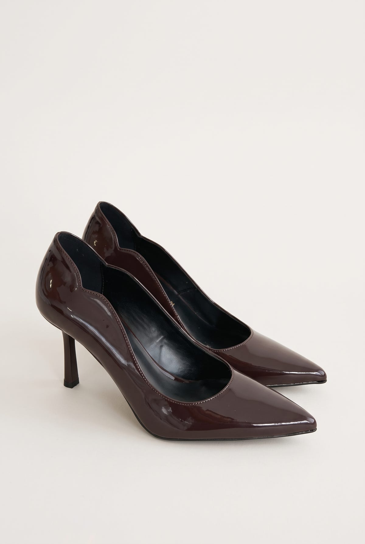 Angled view of a pair of dark brown patent pumps with scalloped cut sides and pointed toes