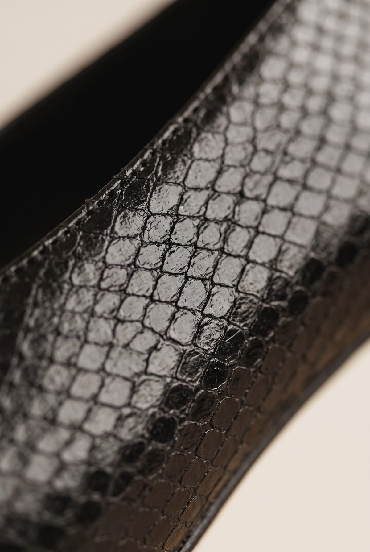 Close-up of black snake-effect leather texture on a pump with a glossy finish and dark edge stitching