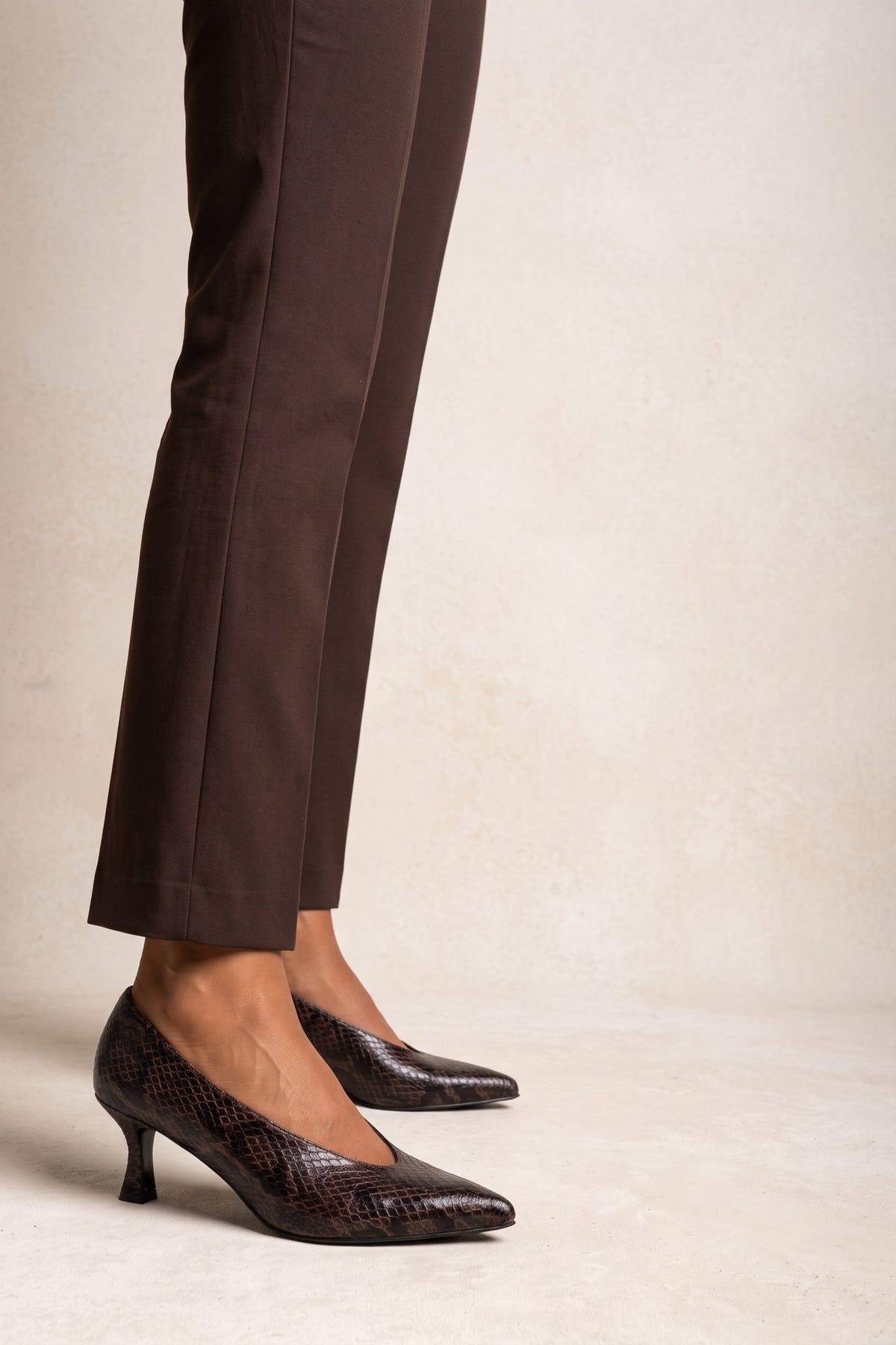 Model in brown trousers wearing brown snake-print kitten heel pumps, seen from the side