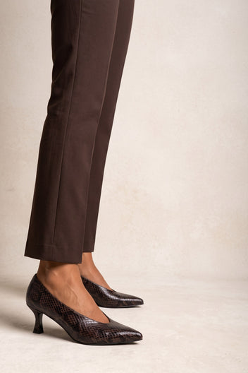 Model in brown trousers wearing brown snake-print kitten heel pumps, seen from the side