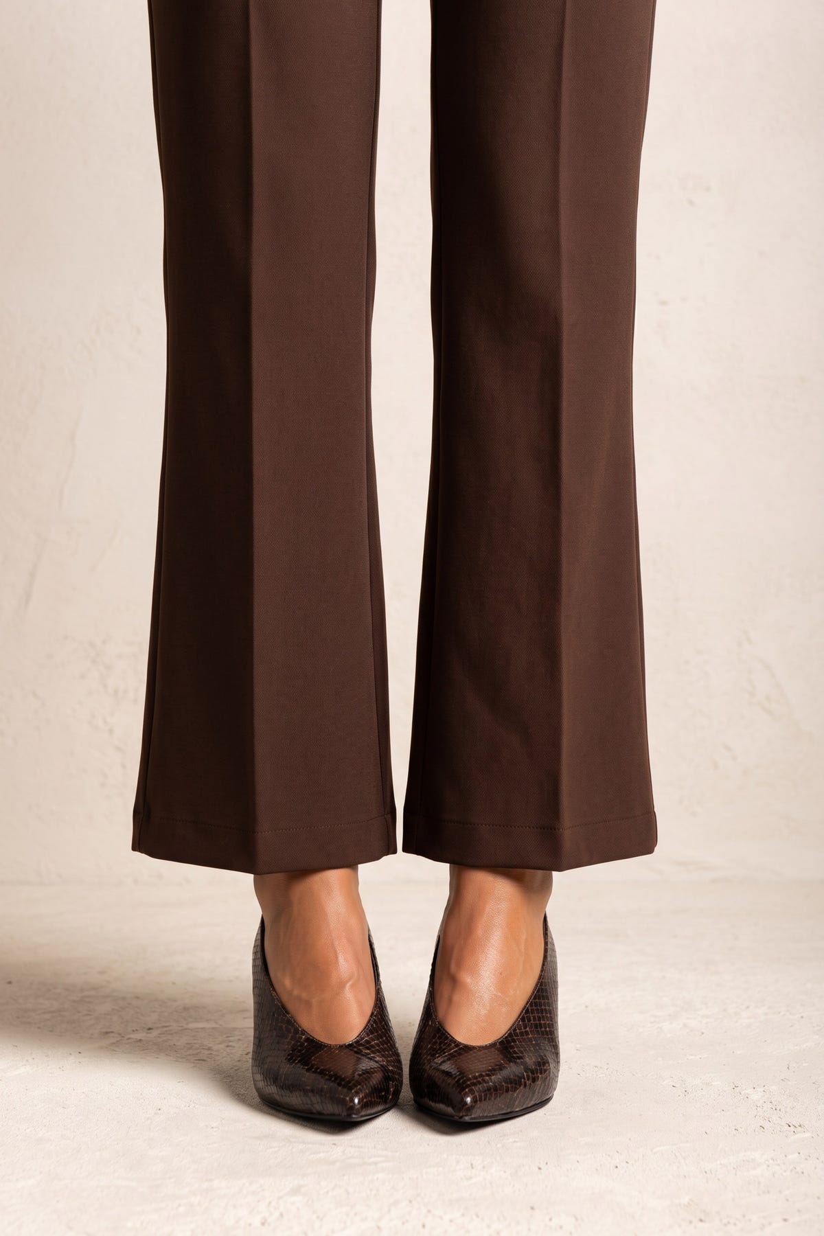 Model wearing brown snake-print kitten heel pumps with brown flared trousers, front view of the feet
