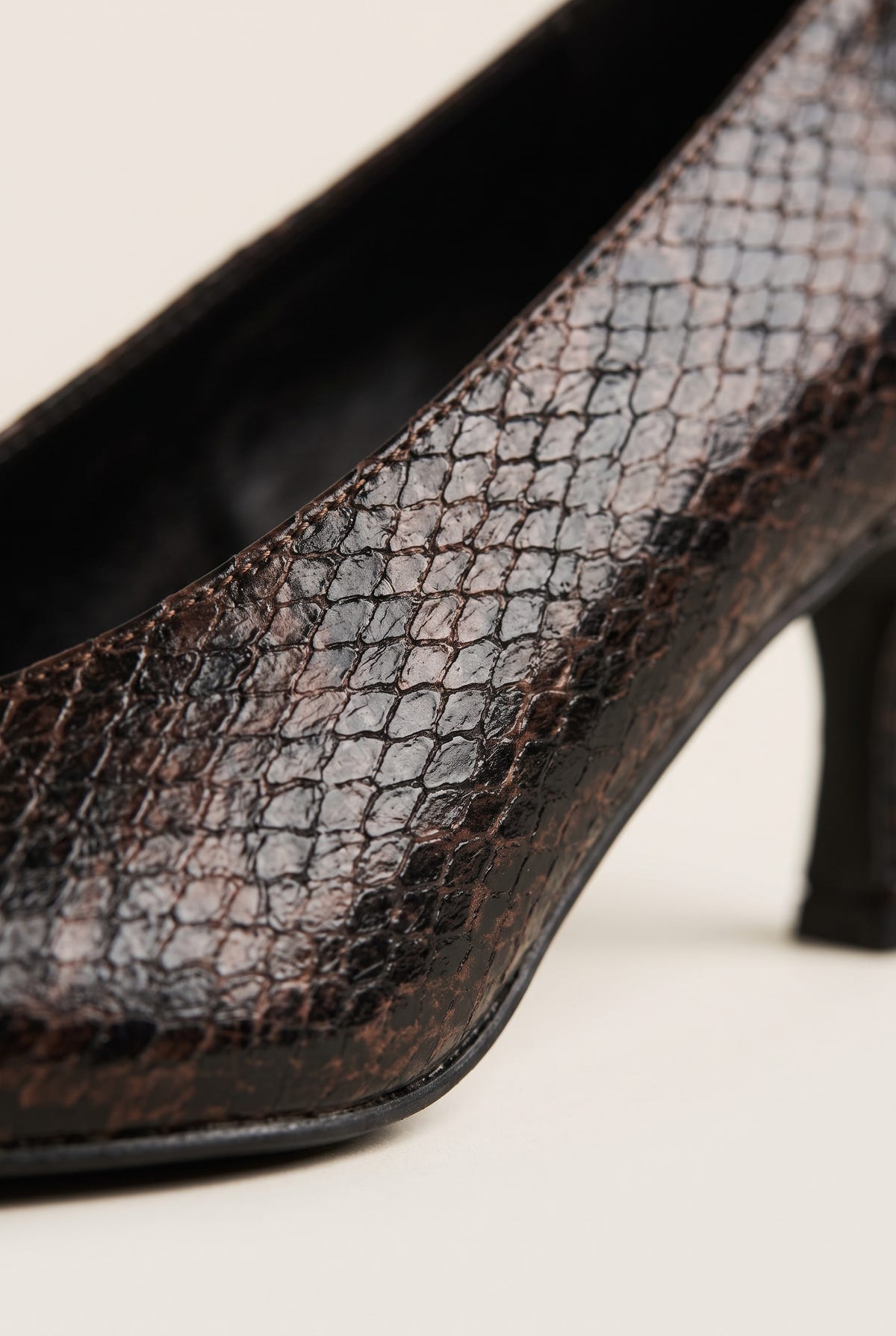 Close-up of brown snake-print leather on a pump with a slim heel and smooth black sole edge