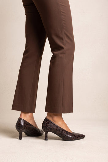 Model in brown straight-leg trousers wearing brown snake-print pointed kitten heel pumps, side view