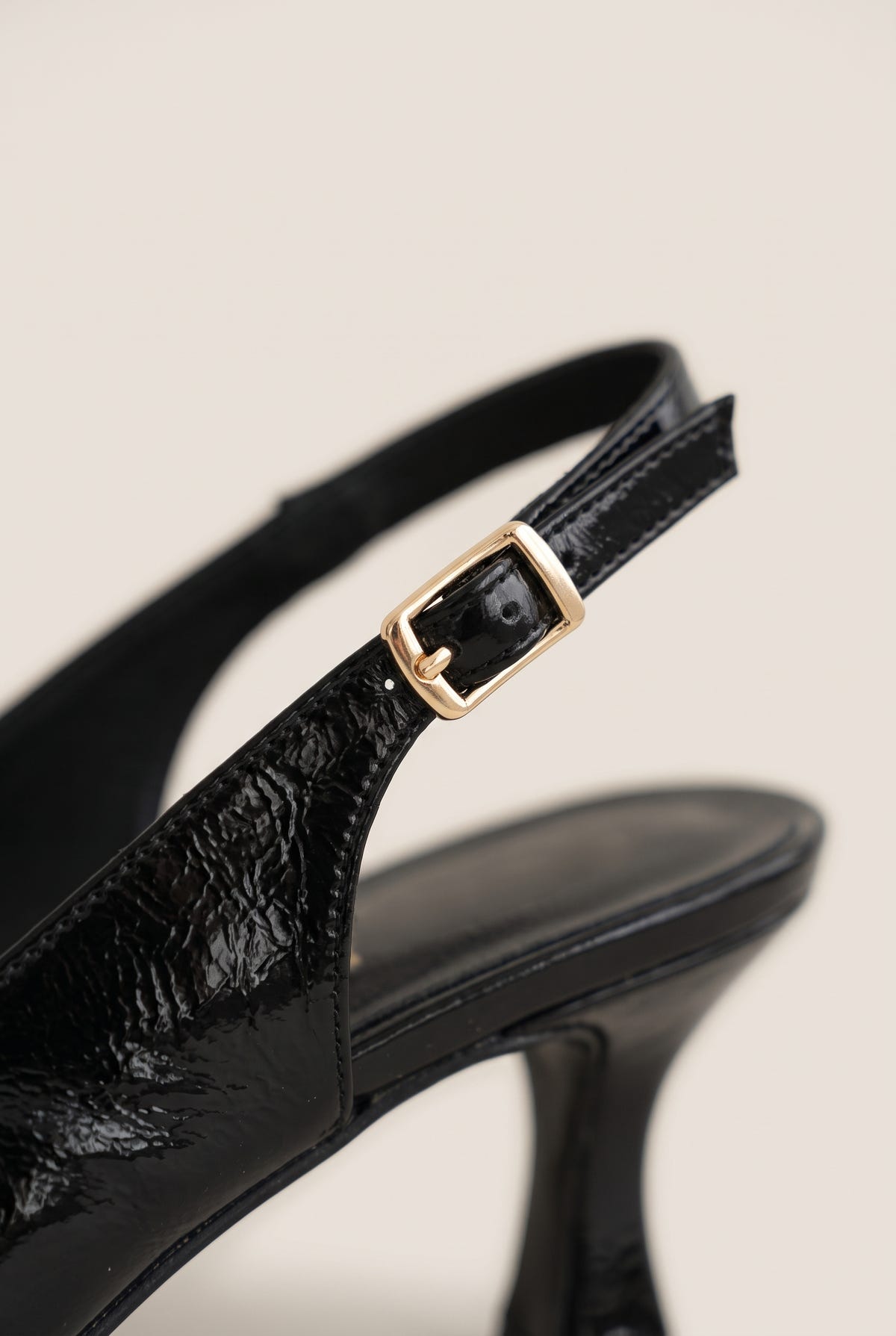 Close-up of black patent slingback showing the glossy finish, gold-tone buckle and slim kitten heel