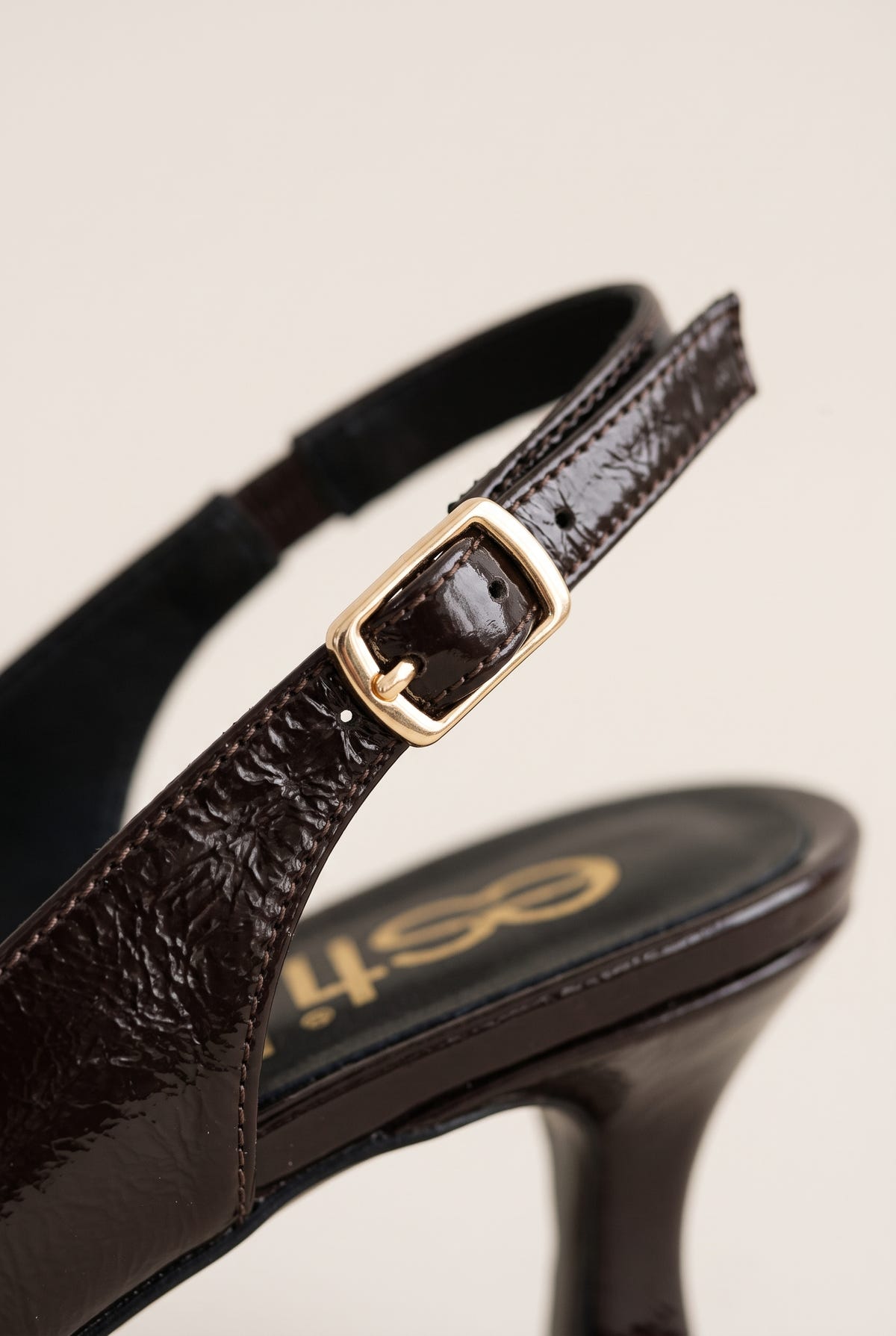 Close-up of brown crinkled patent strap with a gold-tone buckle and a slim kitten heel