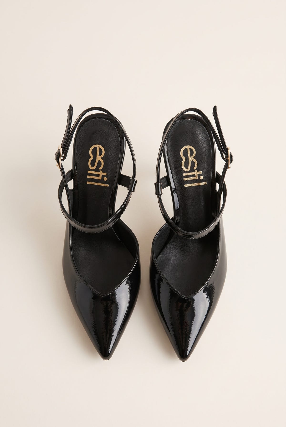 Top view of a pair of black patent pointed slingback pumps with ankle straps and gold buckles