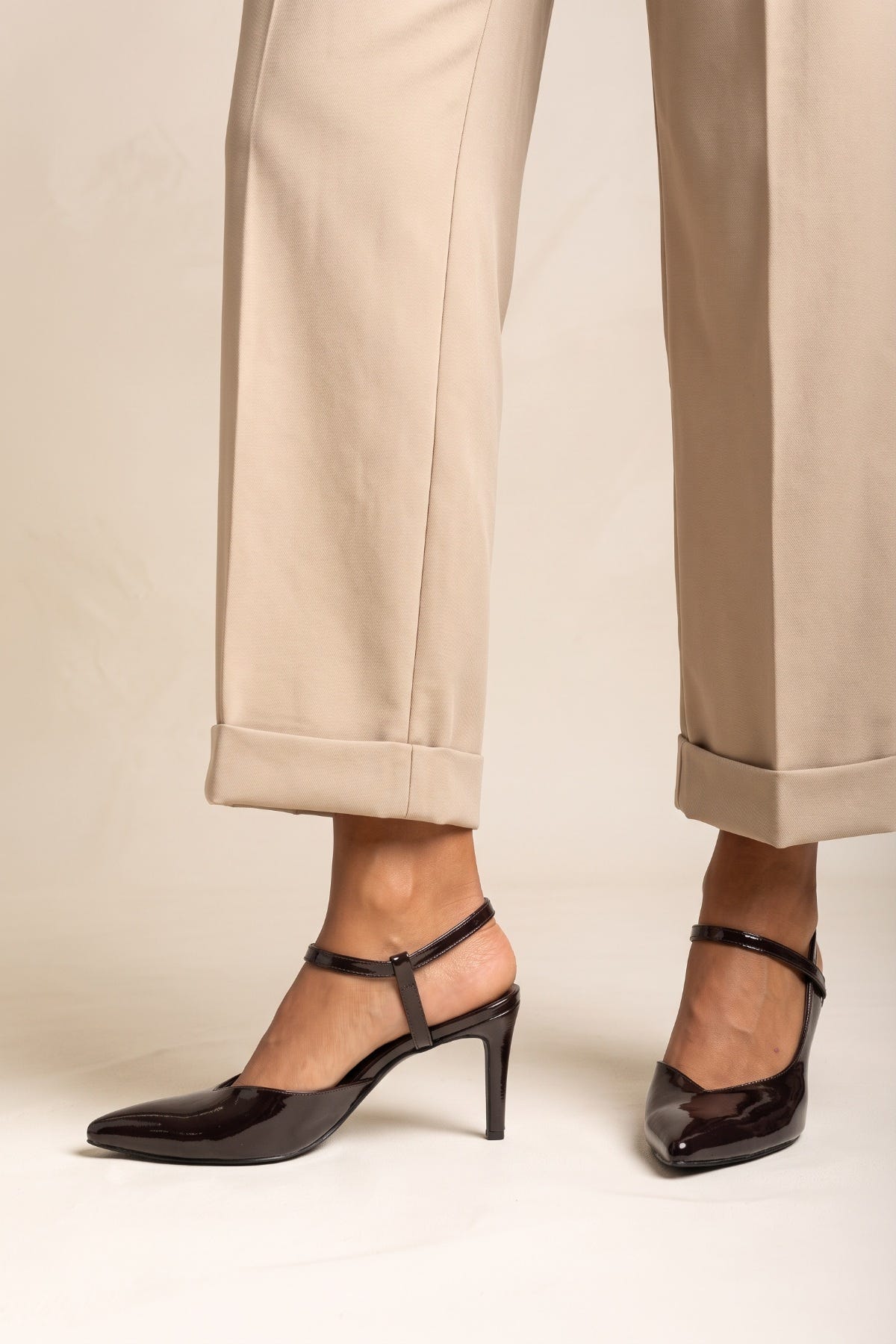 Model in beige cuffed trousers standing in brown patent slingback pumps with feet apart and straps visible