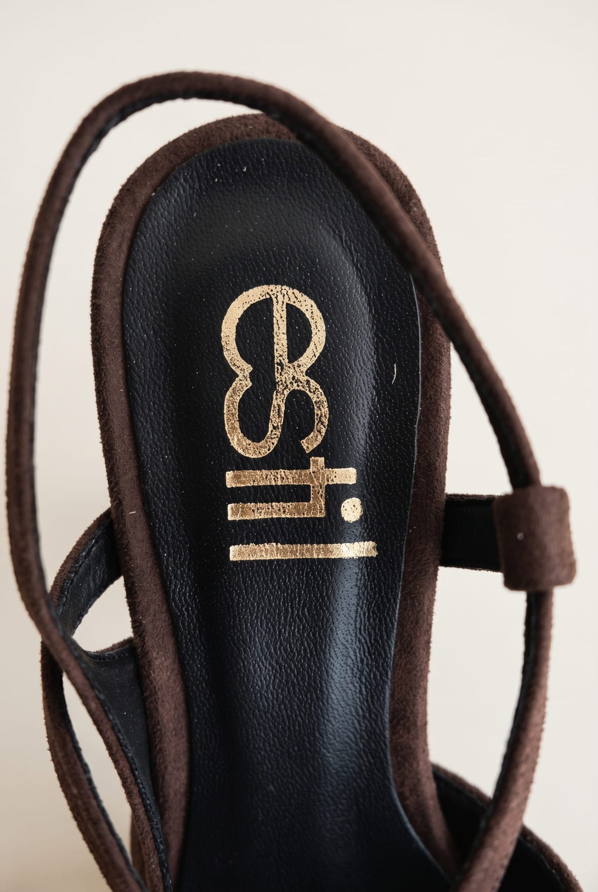 Close-up of brown suede slingback strap curving past a dark leather insole with gold-toned emblem