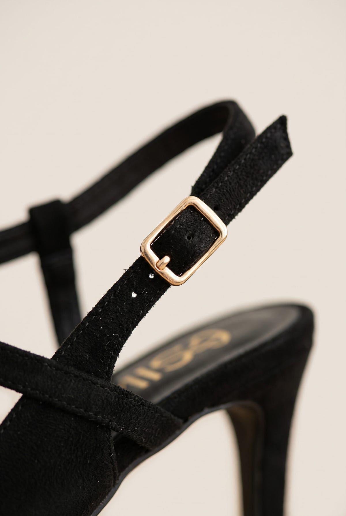 Close-up of black suede ankle strap with gold-toned buckle curving over a pointed slingback shoe