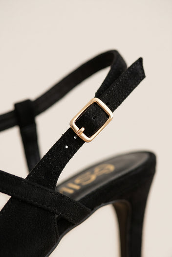 Close-up of black suede ankle strap with gold-toned buckle curving over a pointed slingback shoe
